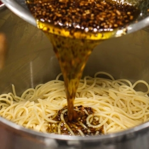 adding spice-infused olive oil to spaghetti pasta