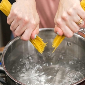 breaking spaghetti and adding to a large pot of boiling water