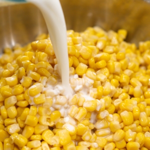 pouring whole milk in a skillet with corn to make homemade creamed corn