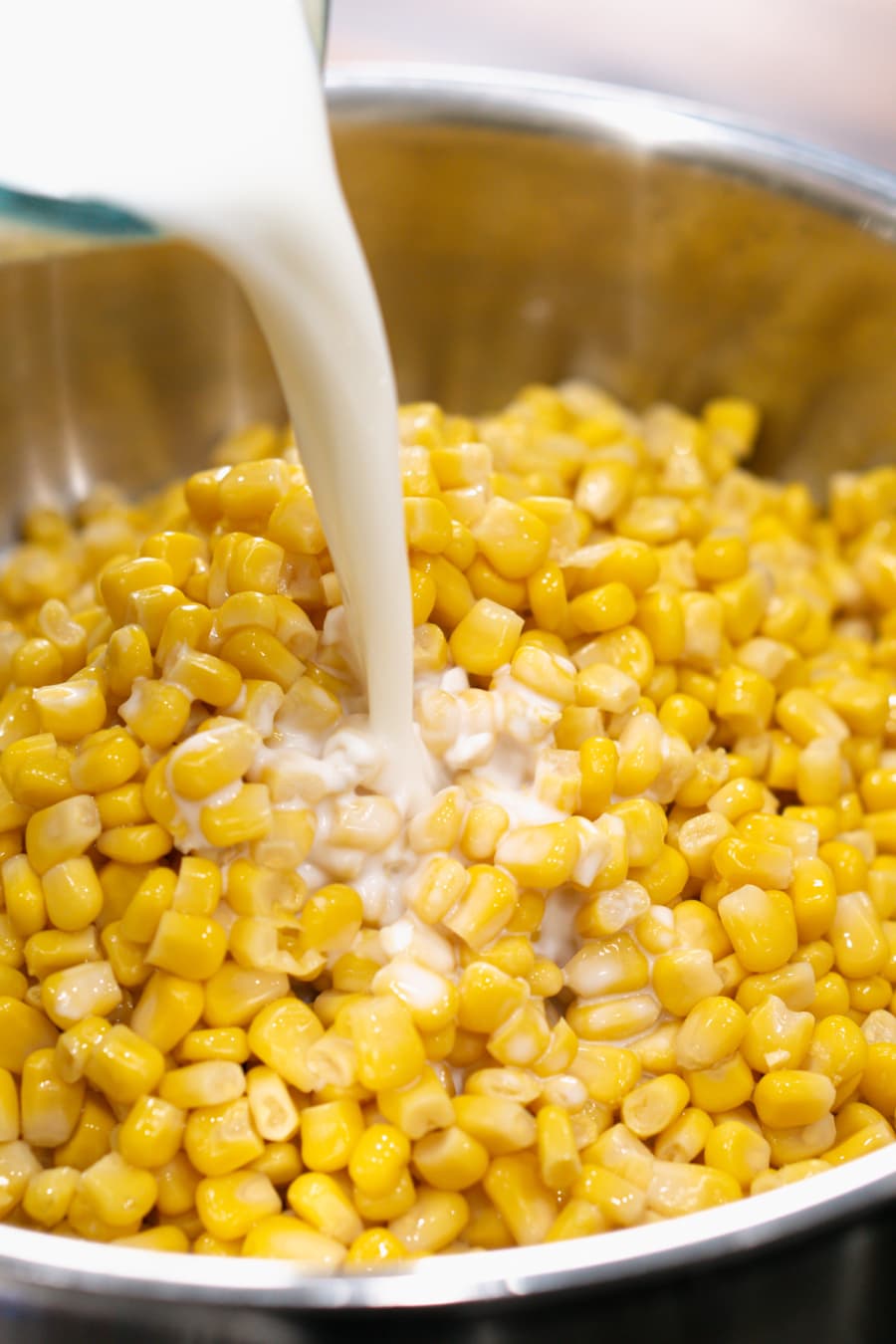 pouring whole milk in a skillet with corn to make homemade creamed corn