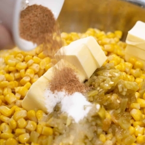 adding diced green chiles, butter, sugar, and creole seasoning to corn in a skillet