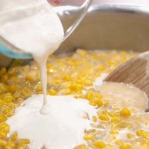 adding a mixture of heavy cream and flour to a skillet full of creamed corn