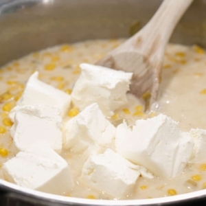 adding cream cheese to creamed corn in a skillet