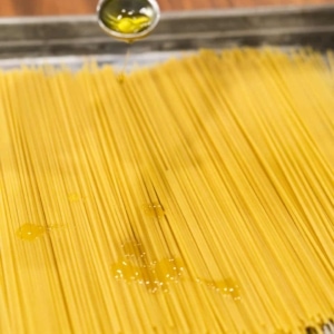 pouring a teaspoon of olive oil over spaghetti pasta