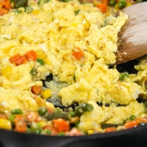 making scrambled eggs in a cast iron skillet using a wooden spoon