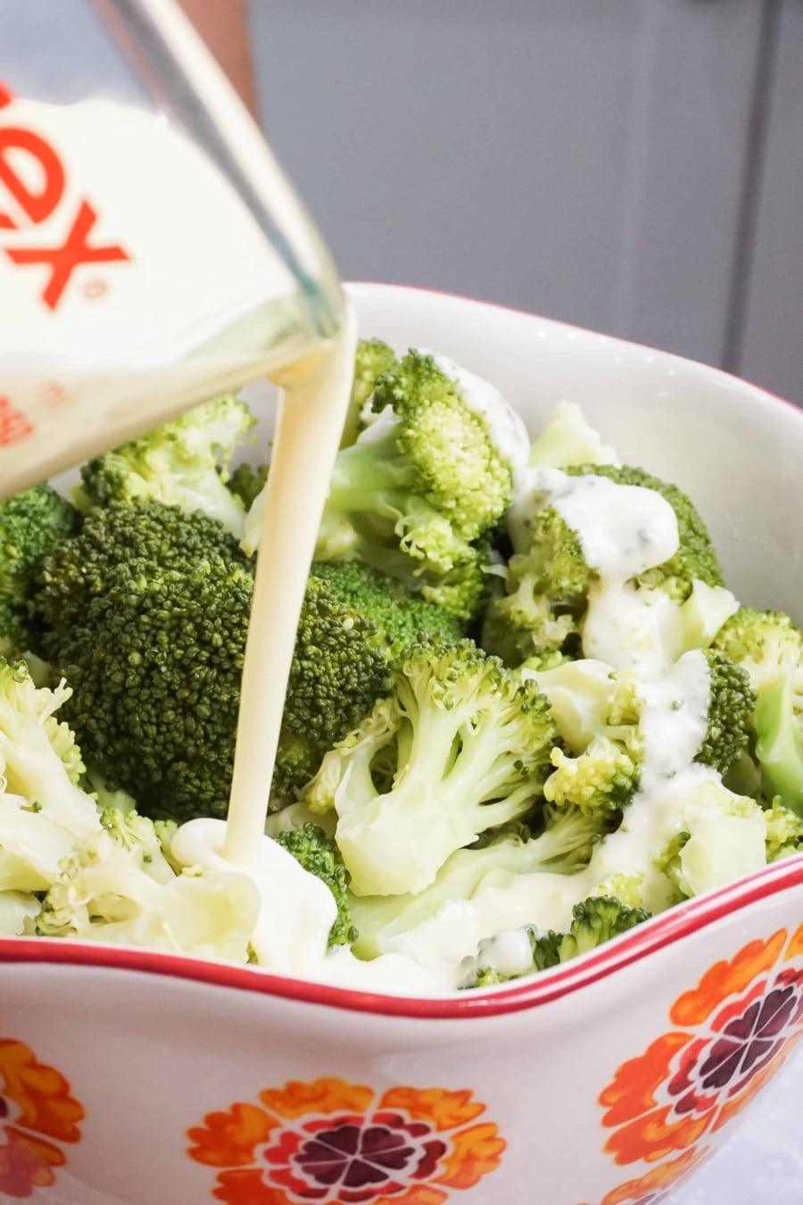 pouring a creamy lemon butter sauce over broccoli in a large bowl