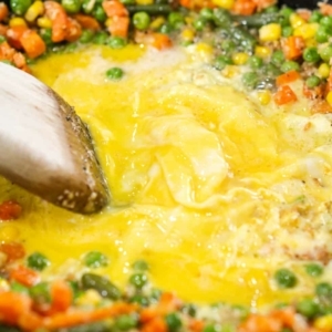 cooking scrambled eggs in the center of a skillet using a wooden spoon