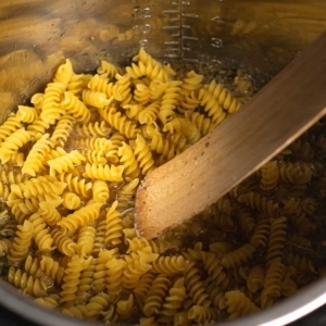 pushing pasta down into chicken stock to make tuscan chicken pasta in the instant pot