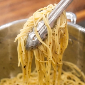 using a pair of tongs to serve spicy spaghetti aglio e olio