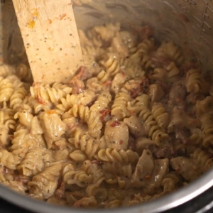 mixing cream cheese and parmesan cheese into pasta in the instant pot to make tuscan chicken pasta