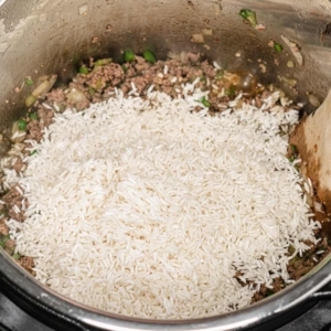 a mound of long grained white rice sitting on top of a mixture of cajun seasoned ground beef, ground pork sausage, and diced vegetables in the instant pot