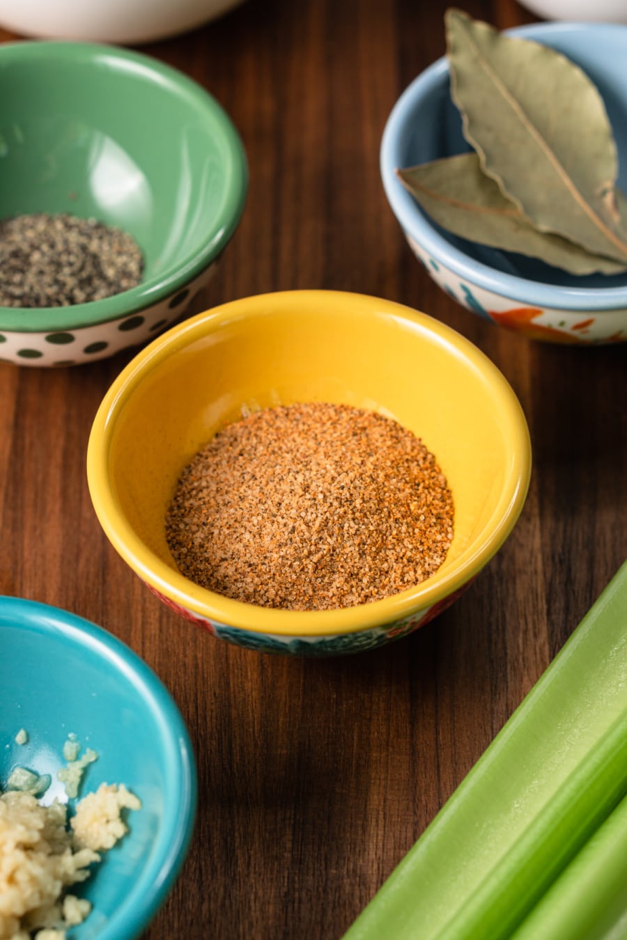 a set of mini prep bowl filled with herbs and spices including creole seasoning, bay leaves, ground black pepper, and minced garlic