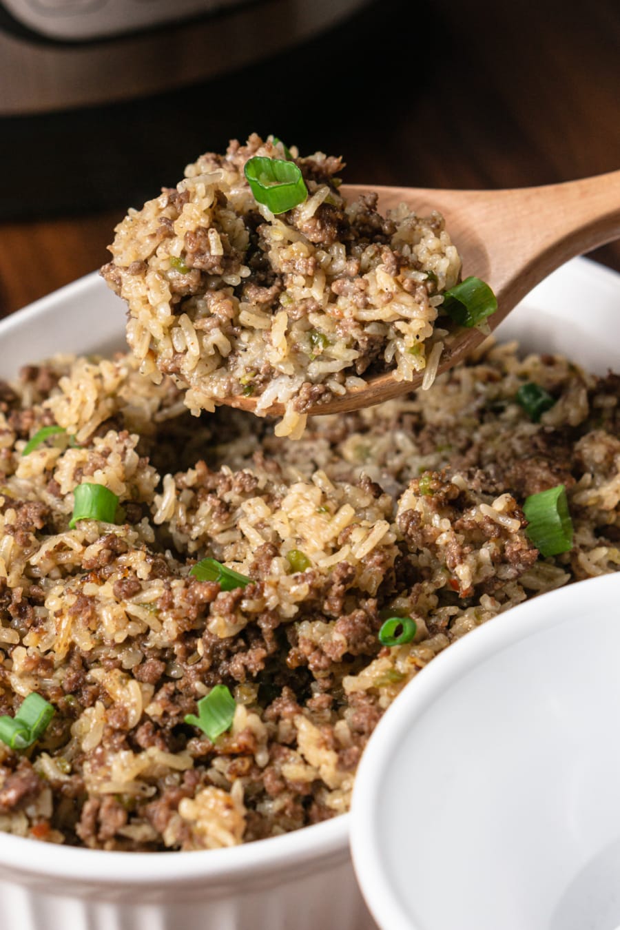 a wooden spoon scooping out dirty rice from a baking dish to serve in a small bowl