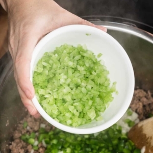 adding a small bowl of diced celery to a mixture of ground sausage and lean ground beef in the instant pot pressure cooker