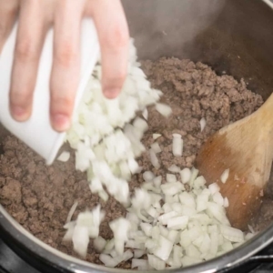 adding a small bowl of diced onion to a mixture of ground beef and ground sausage in the instant pot pressure cooker