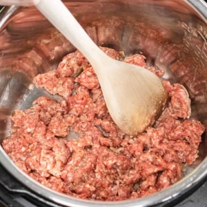 breaking apart ground pork sausage, with a large wooden spoon as it cooks in the instant pot pressure cooker