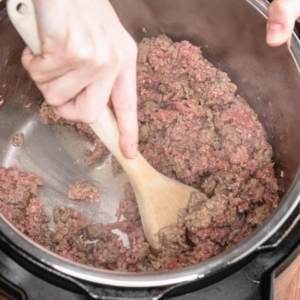 mixing and tossing lean ground beef and ground pork sausage with a large wooden spoon while they cook in the instant pot electric pressure cooker