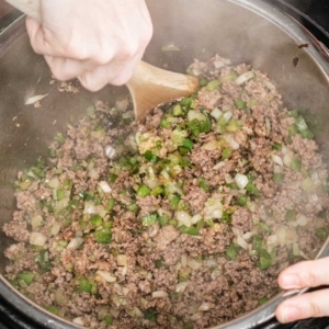 mixing lean ground beef and ground pork sausage with diced vegetables and cajun spices with a large wooden spoon as they cook in the instant pot pressure cooker