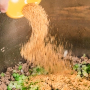 sprinkling creole seasoning over a mixture of ground beef, ground pork, and diced vegetables in the instant pot pressure cooker