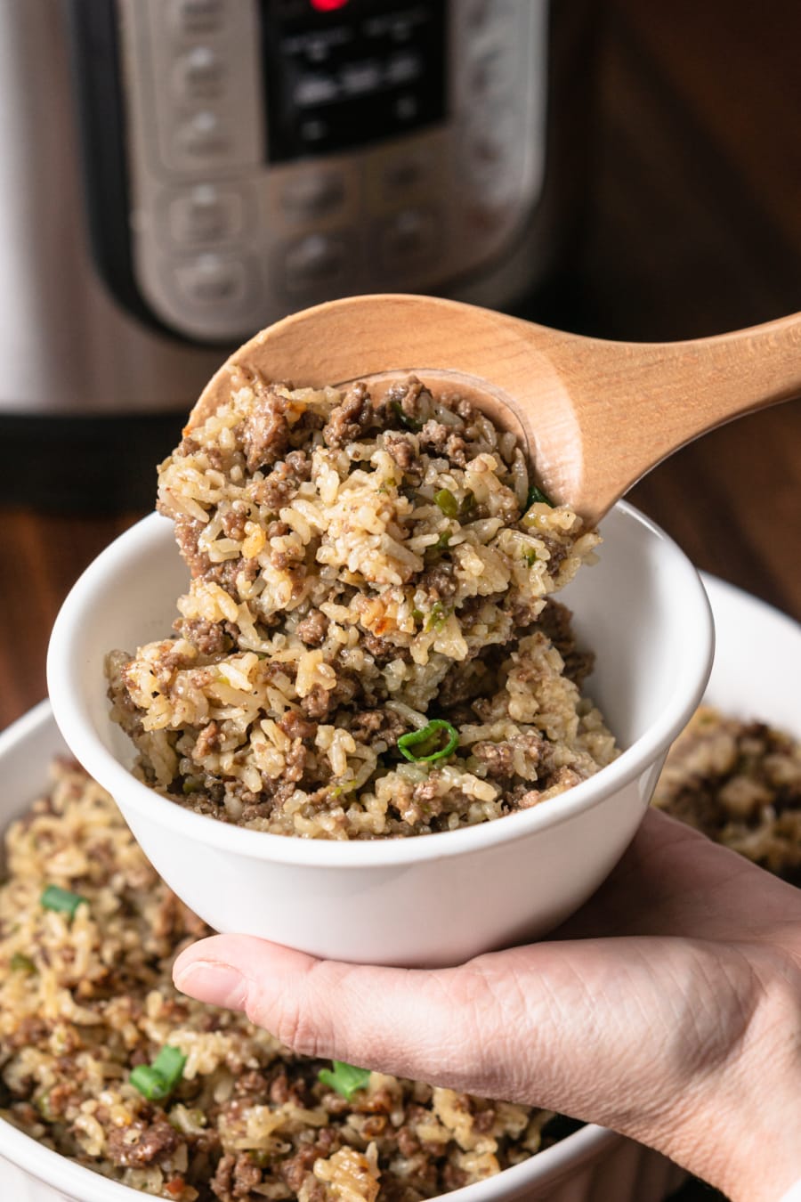 using a wooden spoon to add a scoop of dirty rice to a small bowl