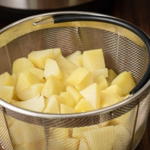 a wire mesh basket filled with cooked potatoes sitting on the counter