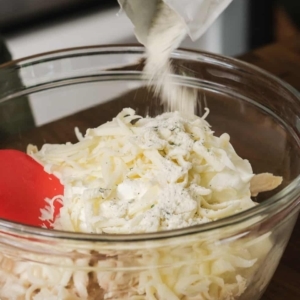 pouring a packet of Hidden Valley Ranch Dressing seasoning over the ingredients for buffalo ranch chicken dip in a large glass mixing bowl