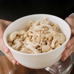 holding a small white prep bowl filled with shredded chicken in both hands