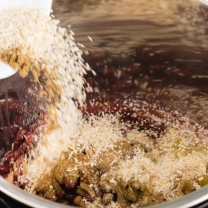 adding a bowl of spices over the ingredients for red beans and rice in the instant pot