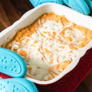 using some large oven mitts to handle a hot casserole of buffalo ranch chicken dip fresh out of the oven and setting it on a trivet on the counter top