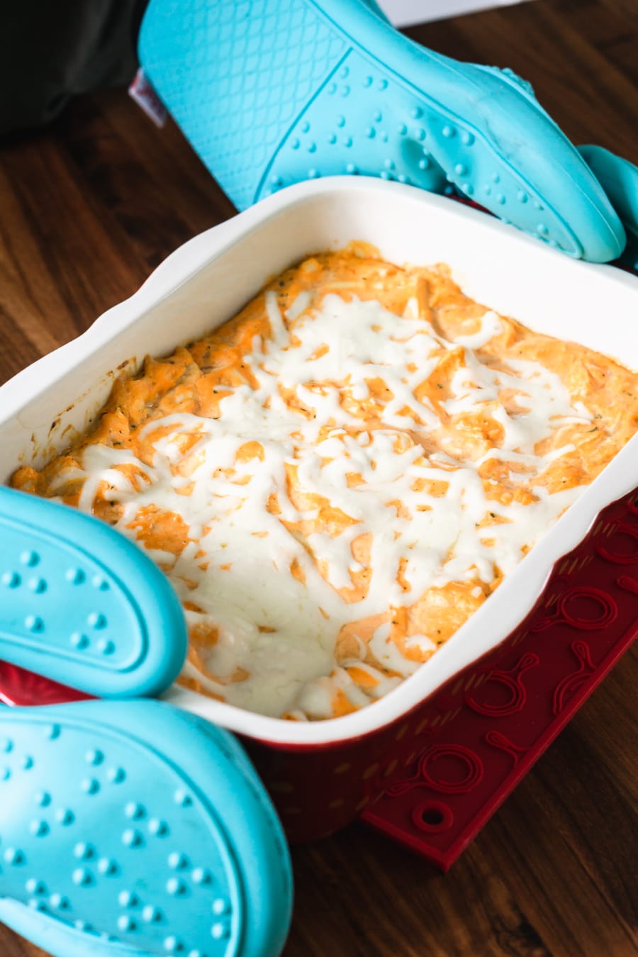 using some large oven mitts to handle a hot casserole of buffalo ranch chicken dip fresh out of the oven and setting it on a trivet on the counter top