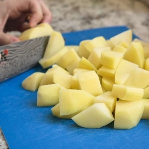 chopping potatoes with a knife on a cutting board full of chopped potatoes