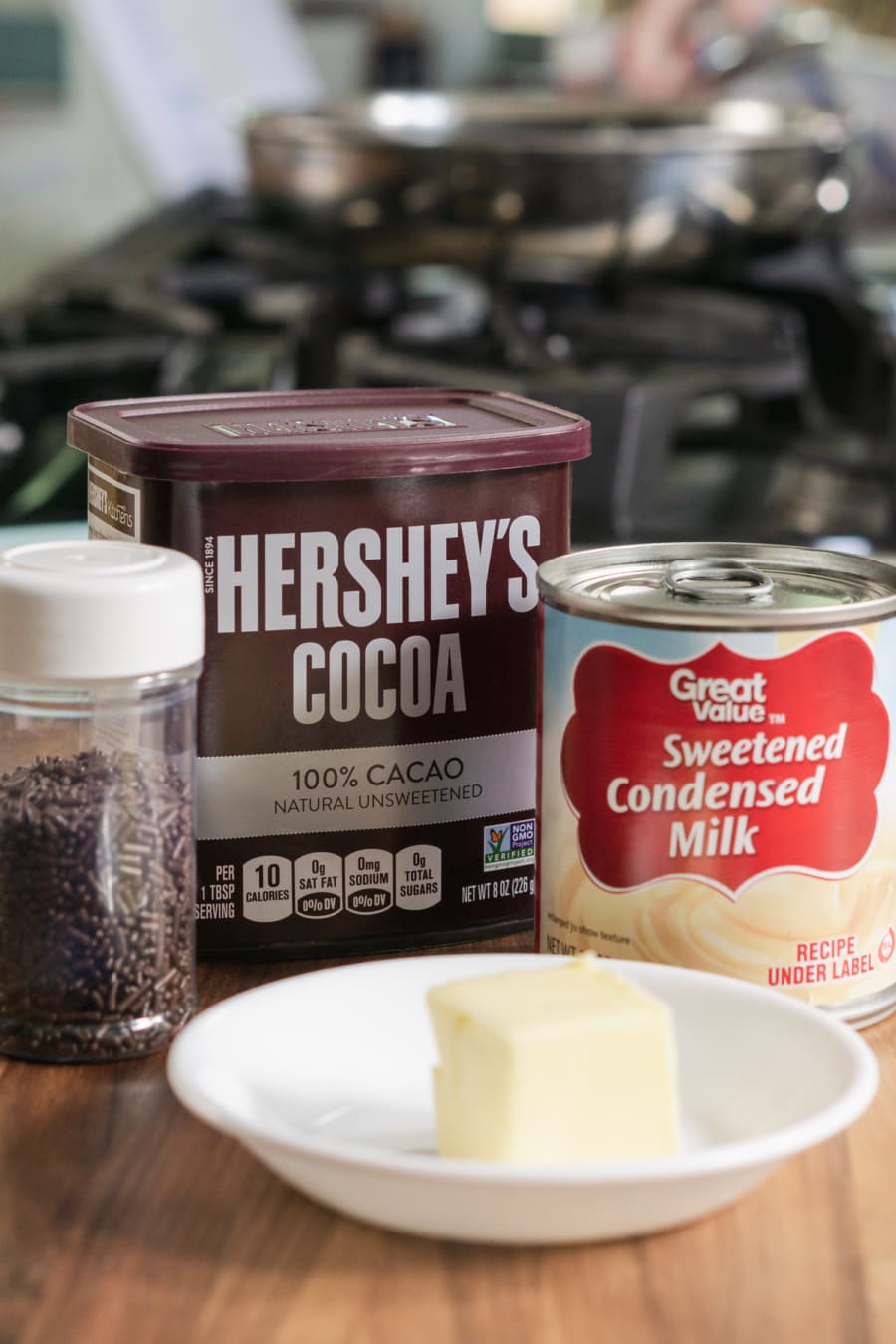 the ingredients for chocolate brigadeiros sitting on the counter including Hershey's cocoa, sweetened condensed milk, butter, and chocolate sprinkles