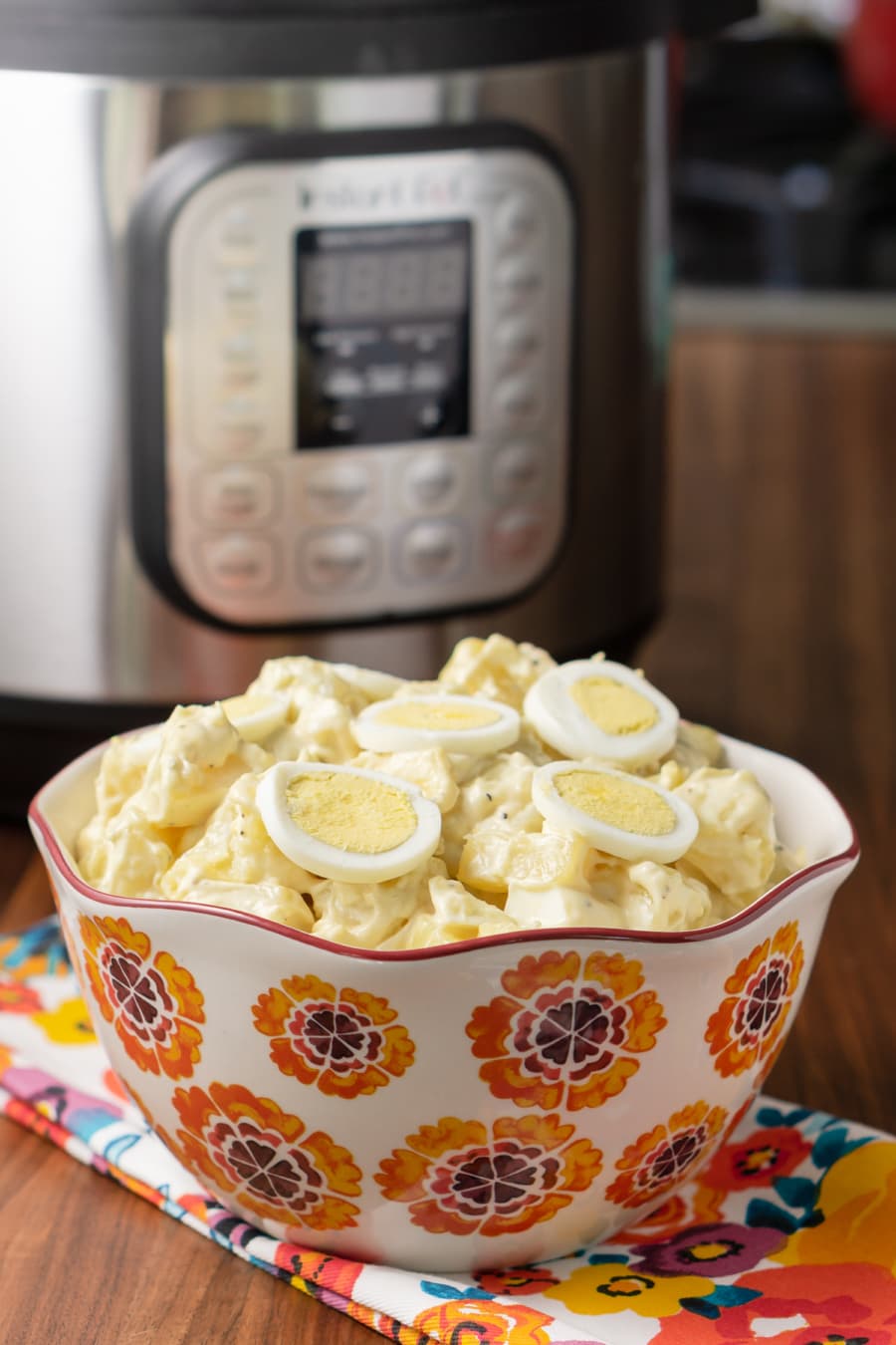 a serving bowl filled with potato salad and topped with slices of egg sitting in front of the instant pot