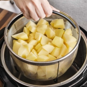 lowering a mesh basket filled with chopped potatoes into the instant pot