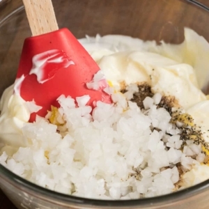 sour cream, mayonnaise, mustard, Worcestershire sauce, salt, pepper, and onion in a mixing bowl, with a spatula