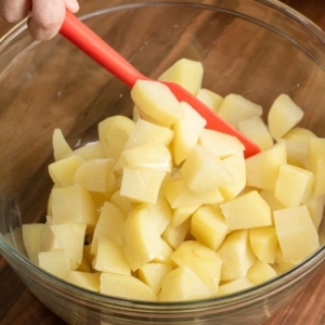 mixing cooked chopped potatoes with vegetable oil in a large mixing bowl