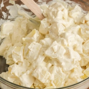 mixing chopped potatoes and eggs with a creamy sauce in a large mixing bowl