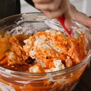 mixing the ingredients for buffalo ranch chicken dip in large glass mixing bowl