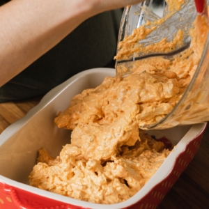 pouring buffalo ranch chicken dip into a baking dish