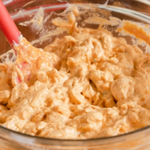 a large glass mixing bowl filled with a creamy orange dip made with a mix of shredded chicken, cheese, and buffalo sauce