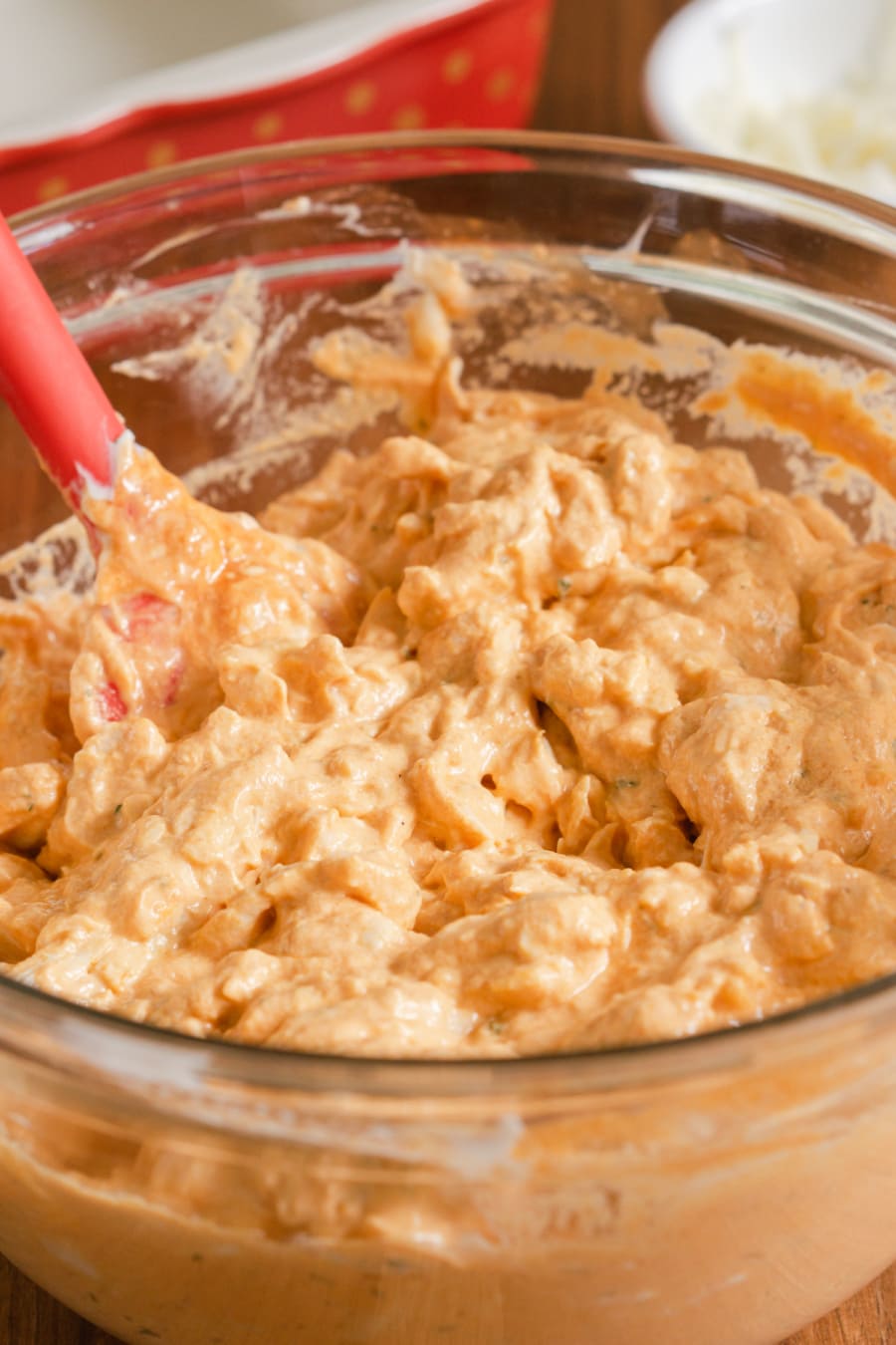 a large glass mixing bowl filled with a creamy orange dip made with a mix of shredded chicken, cheese, and buffalo sauce