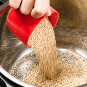 pouring a cup of quinoa into an electric pressure cooker