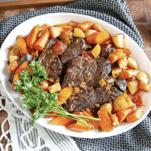 a plate of coca cola pot roast surrounded by carrots and potatoes