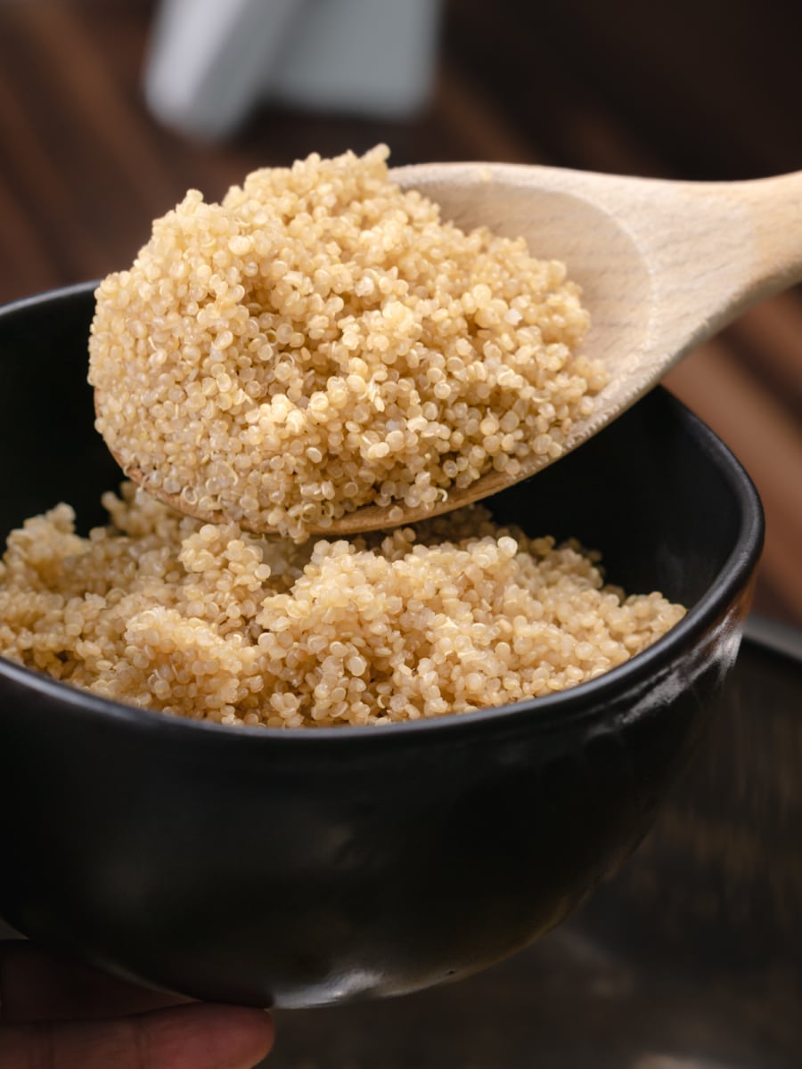 a scoop of quinoa in a wooden spoon being added to a bowl of quinoa