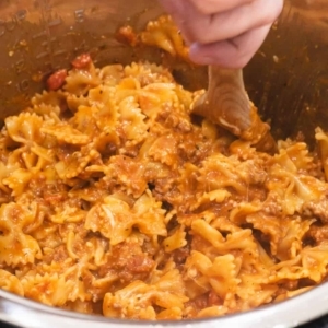 mixing cheeses into cooked bowtie pasta with meat and sauce in the instant pot