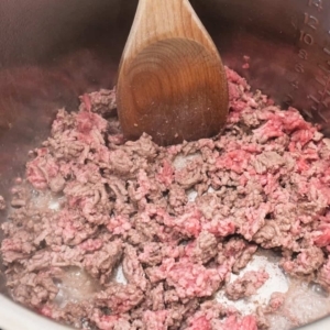 using a large wooden spoon to saute ground beef in the instant pot