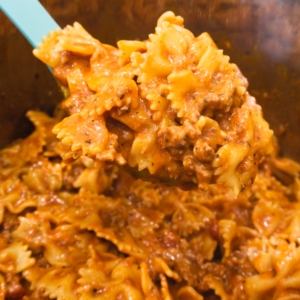 a large serving spoon filled with bowtie pasta with meat and a red sauce being served from the instant pot