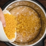 pouring elbow pasta into chicken stock in the instant pot