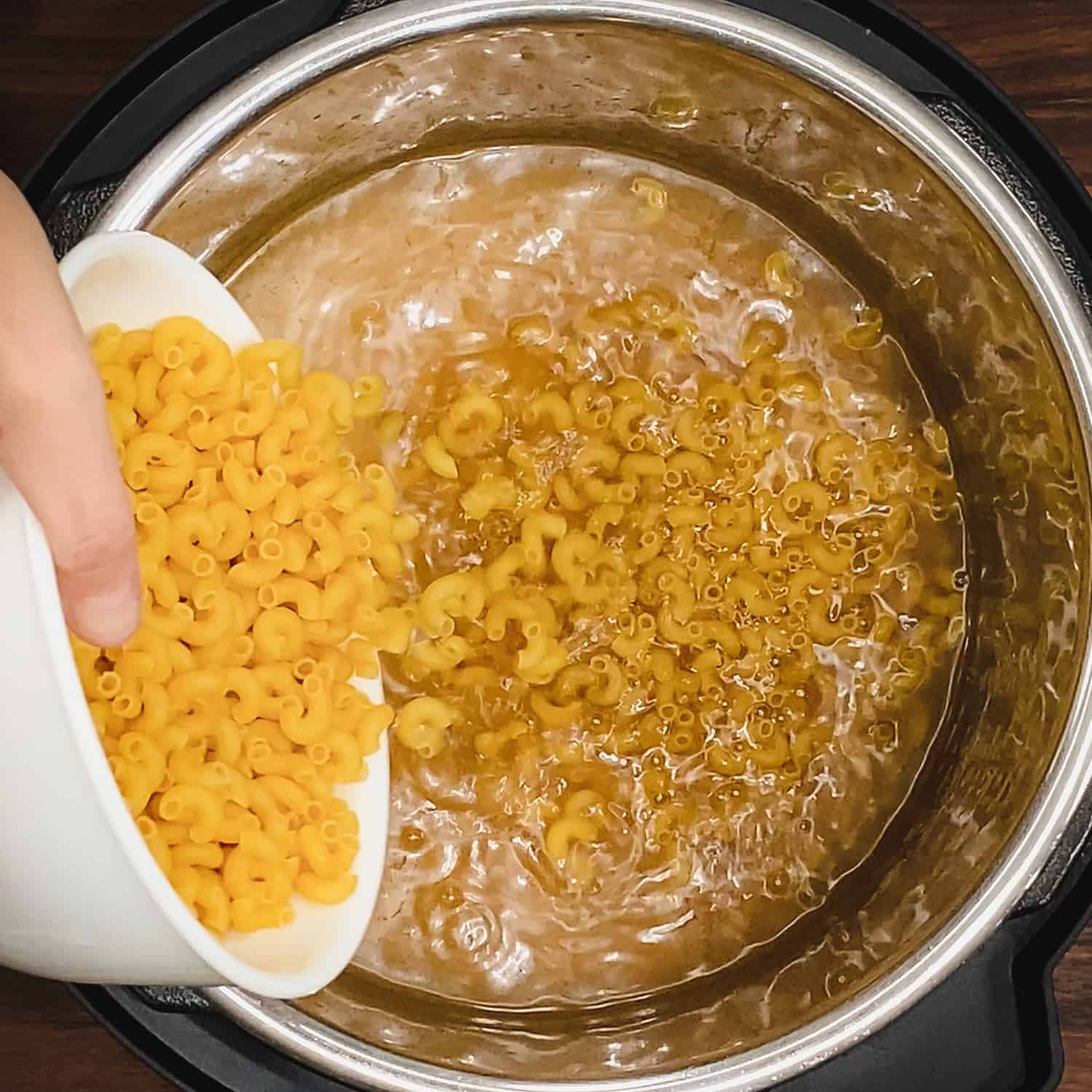 pouring elbow pasta into chicken stock in the instant pot