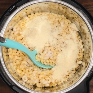 adding parmesan cheese to cooked elbow pasta and mushroom soup in the instant pot